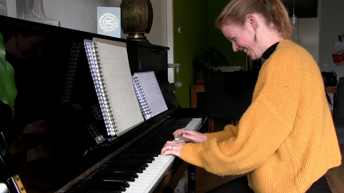 Lieke Brouwer speelt piano. Op de piano staat twee boekjes met braillebladmuziek.